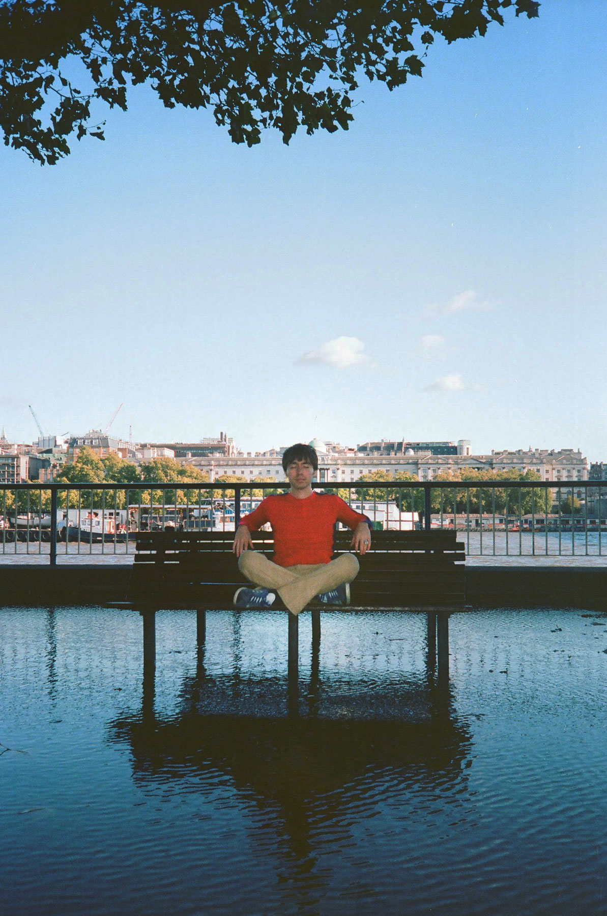 Campaign photograph — Matt cross-legged on a bench above the Thames